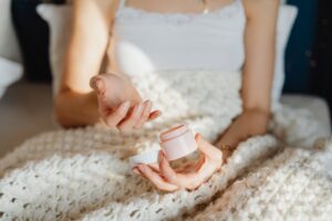 A person uses moisturizer while wrapped in a cozy wool blanket indoors