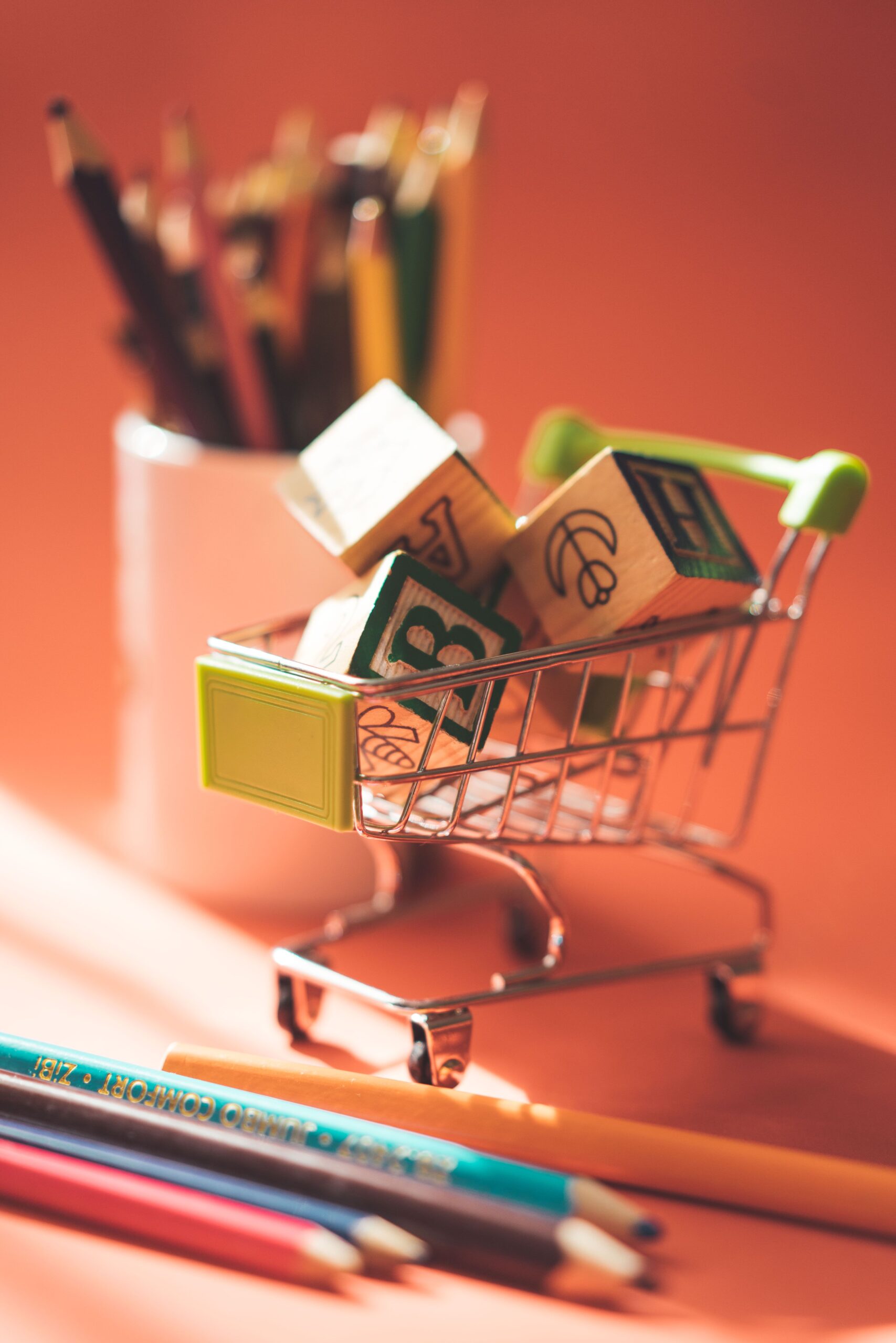 A miniature shopping cart filled with alphabet blocks and colored pencils, representing back-to-school shopping
