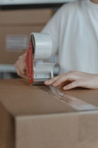 Person sealing a cardboard box with a tape dispenser