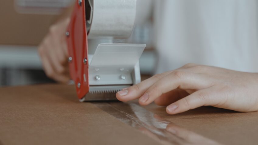 Person sealing a cardboard box with a tape dispenser